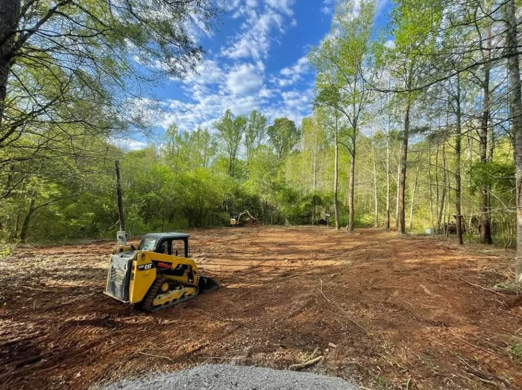 Better Way Land Management LLC crew performing land management in Toledo, compact track loader clearing wooded property with excavator in background